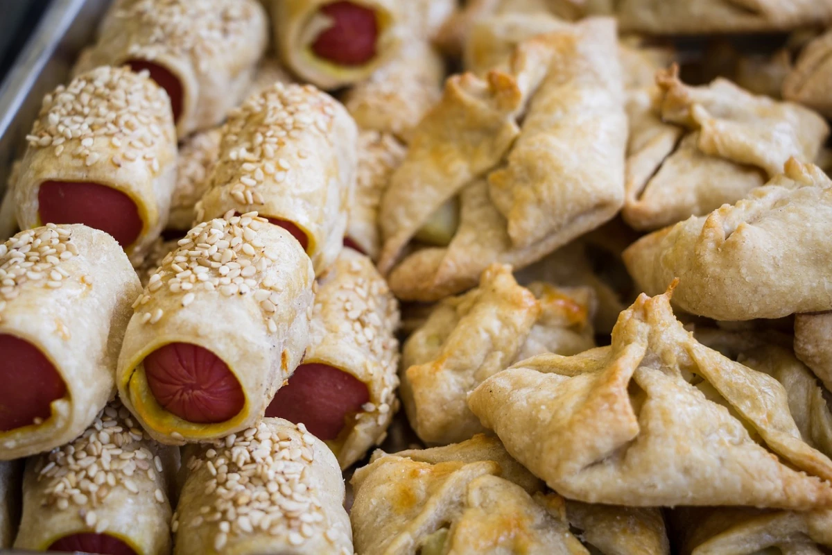 Blacha pełna przekąsek z parówek zawiniętych w ciasto francuskie, posypanych sezamem oraz sakiewek z ciasta nadziewanych farszem